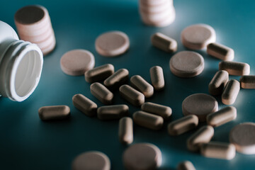 Different types of tablets and capsules scattered on a surface near an open bottle in a well-lit environment