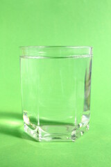 On a green background there is a glass cup with transparent clean drinking water.