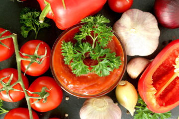  On a black background there is a glass bowl with tomato sauce and vegetables.