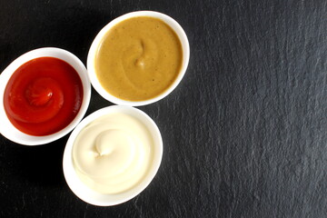Three types of sauces stand in plates on a black background.