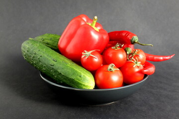 On a black background there is a ceramic plate with a fresh harvest of vegetables.