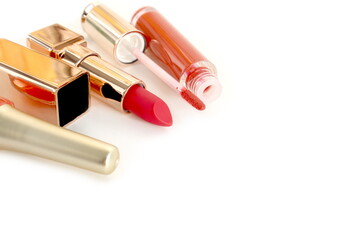 Obraz premium Orange nail polish, lipstick and lip gloss lie on white background with space for text.