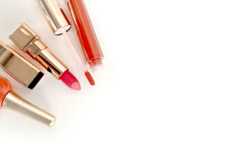 Orange nail polish, lipstick and lip gloss lie on white background with space for text.