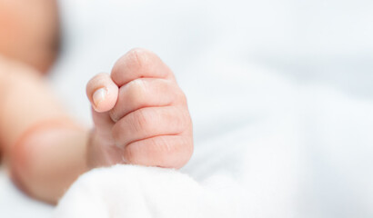 Fist of the baby resting on the white blanket and copy space with selective focus.