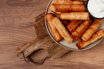 fried spring rolls with cheese, on a wooden background, with cream sauce, no people,