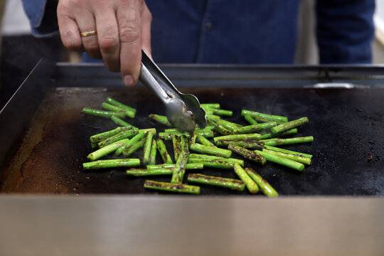 chef cocinero friendo a la plancha unos esp&aacute;rragos verdes y salte&aacute;ndolos con pinzas de cocinar