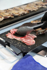 chuletas de cordero friéndose en una plancha grill con el cocinero dándoles la vuelta para freír con una pinza de cocina
