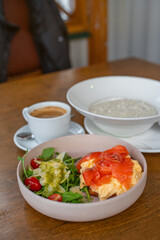 Delicious healthy breakfast spread featuring creamy oat porridge, scrambled eggs topped with smoked salmon, a fresh arugula salad with cherry tomatoes and parmesan, paired with a smooth café crema. 