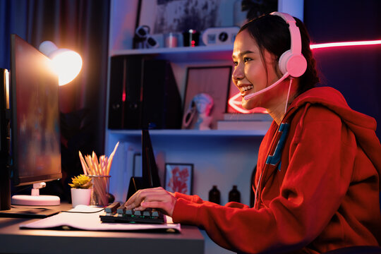 Host channel of young beautiful Asian gaming streamer playing fighting Moba at battle arena game on pc screen with multiplays, wearing pastel headphone at neon digital light modern room. Stratagem.