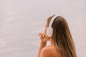 A woman wearing headphones is looking out at the water. The scene is calm and peaceful, with the...