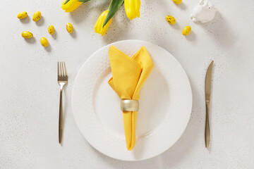 Easter table setting with spring tulips, white plates, bunny, eggs and yellow decoration on white...