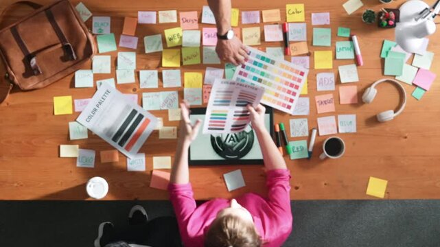 Top view of smart designer holding color palette while project manager looking at design and choosing color for program. Professional businesswoman taking a note while design creative logo. Symposium.