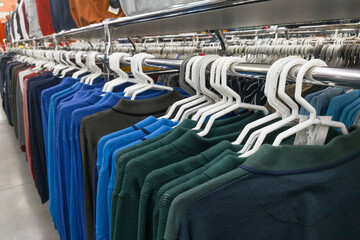 Fototapeta premium A lot of different colored shirts and T-shirts organised in row hanging on white hangers in shopping.Shop with clothes