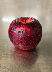 Fresh red apple with water drops on metal surface.
