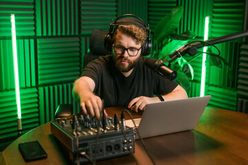 Cheerful young man recording podcast in studio. Confident man with headphones and microphone...
