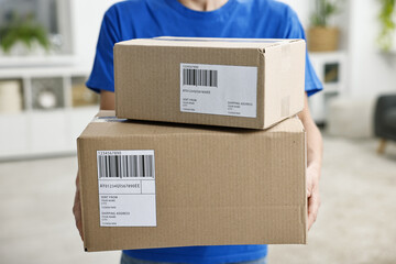 Man holding parcels with shipping labels indoors, closeup