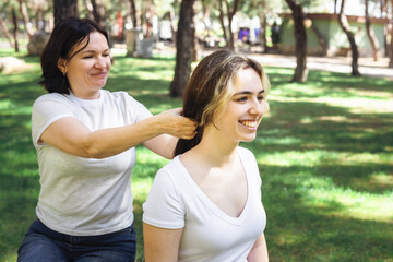 Obraz premium Two women enjoy a sunny afternoon in a park while one styles the other's hair