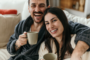 Happy couple laughing and drinking coffee on the sofa