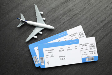 Travel agency. Flight tickets and plane model on dark textured table, flat lay