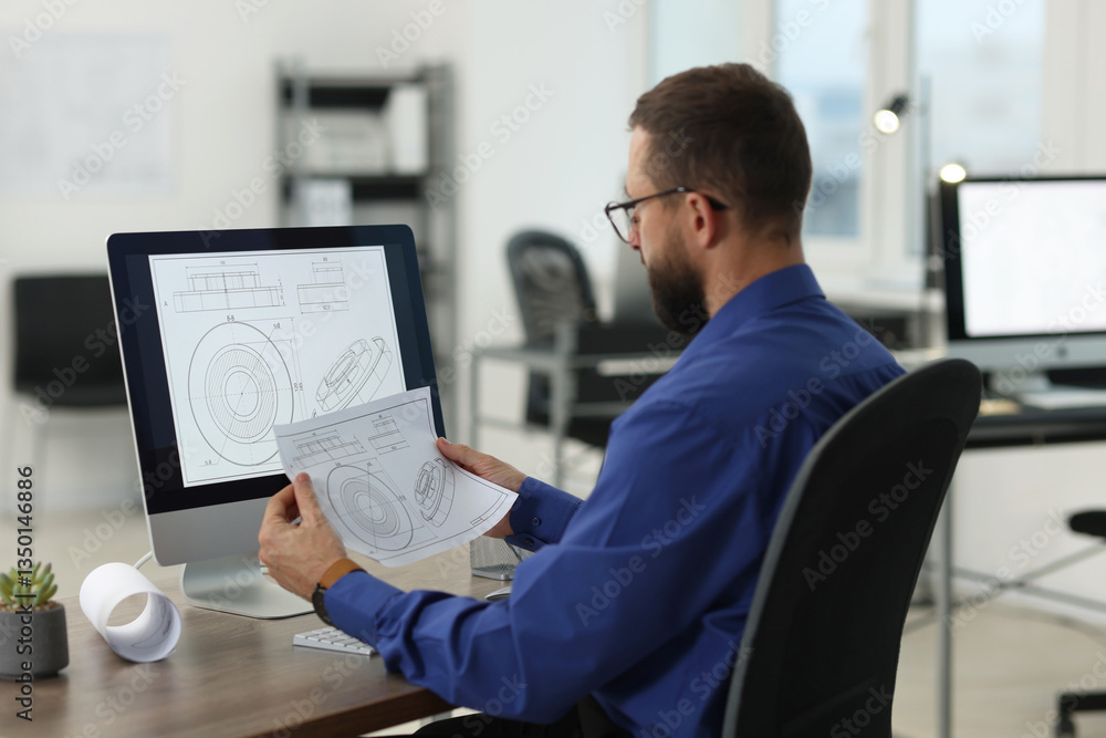 Poster technician making digital engineering drawing on computer at desk in office, back view