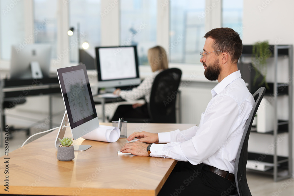 Poster technician making digital engineering drawing on computer at desk in office