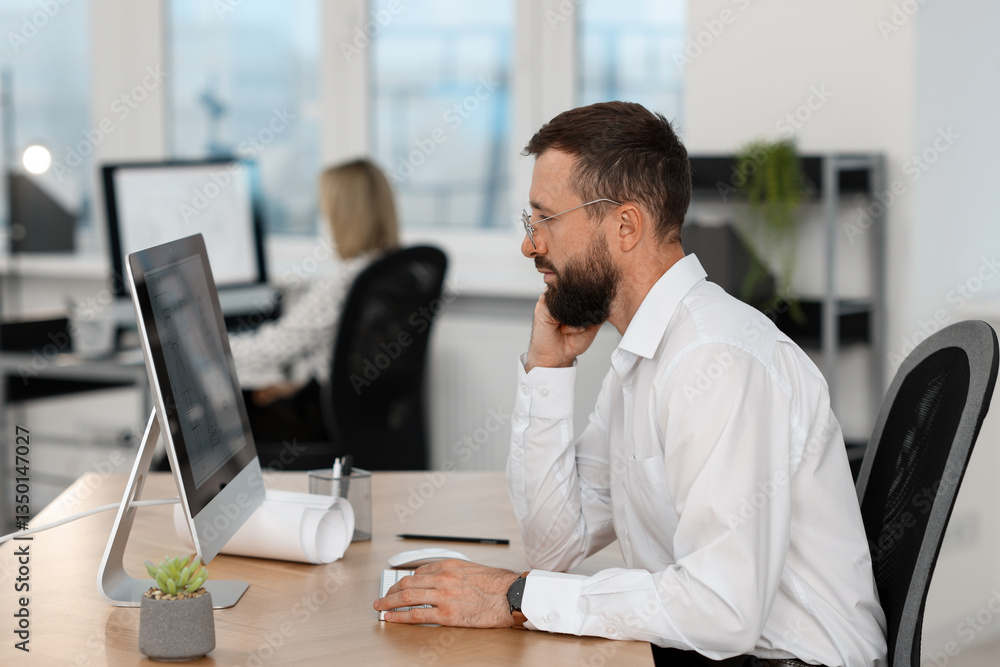 Poster technician making digital engineering drawing on computer at desk in office