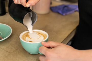 A waitress pouring plant-based cream milk into a cup of coffee in a small hospitality business