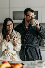 Couple enjoying morning coffee in bathrobes in kitchen