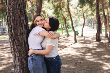 Fototapeta premium Two women embrace in a sunny park surrounded by trees in the afternoon