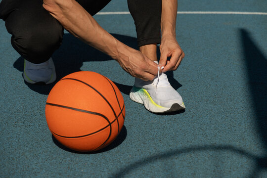 Close up basketball player tying sports shoes in basketball court outdoors. Last preparation. Team game. - Powered by Adobe