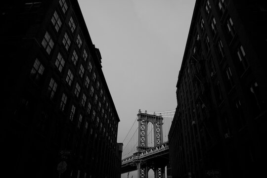 Black and white view of the Manhattan Bridge tower framed by buildings on Washington Street in DUMBO, Brooklyn, New York City