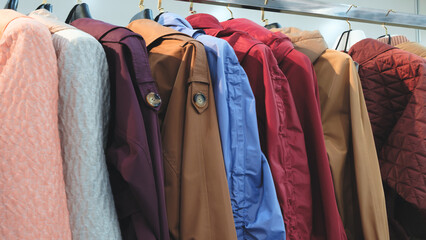 A row of jackets hanging on a rack, including a pink one. The jackets are of different colors and...