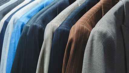 A row of suits hanging on a rack, with the blue suit on the left and the brown suit on the right