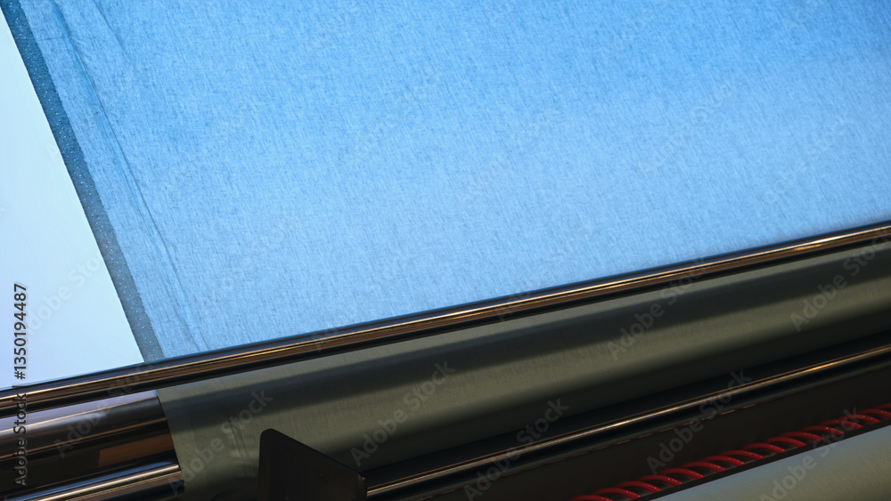Poster a blue fabric is being cut by a machine. the machine is made of metal and has a red rope attached to