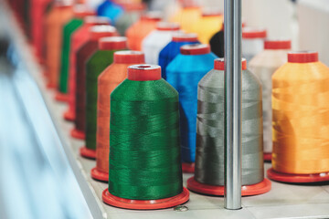A row of colorful spools of thread are displayed on a table. The spools are arranged in a way that they are all visible and easy to access. The colors of the spools are bright and vibrant