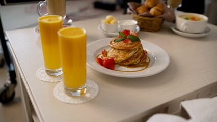 Room service completes breakfast order by bringing plate of syrniki to table already set with pancakes, fruit, juice, and pastries