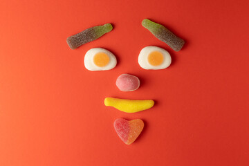 Funny face created with colorful gummy candy on red background