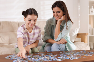 Happy mother and her daughter solving puzzle together at wooden table indoors