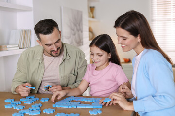 Fototapeta premium Happy parents and their daughter solving puzzle together at wooden table indoors