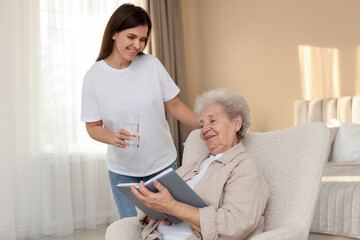 Obraz premium Granddaughter giving glass of water to her grandmother at home. Elderly care