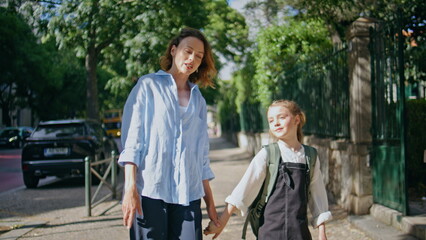 Mother daughter walking sunshine alley closeup. Cute schoolgirl strolling mom