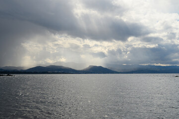 Dramatic clouds gather over a tranquil lake at dusk, creating a serene atmosphere before an evening storm