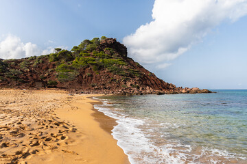 Empty beach Cala del Pilar in Menorca, red mountain and orange sand with crystal clear sea