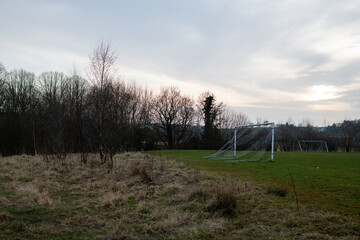 Eham A soccer field with a goal and a few trees in the background. The sky is cloudy and the grass is dry