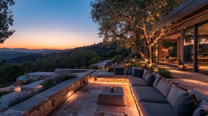 Outdoor stone terrace with cushioned seating, subtle ground lights, and a twilight view