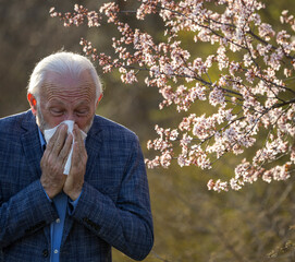 Senior man having allergy symptoms beside blooming tree