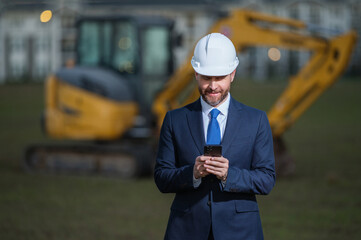 Buider man in suit and hardhat. Construction investor. Business man investor in front of construction site. Successful investor. Handsome man in suit and hardhat at building construction.