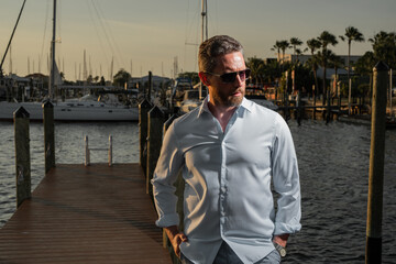 Portrait of handsome confident stylish man in yacht. Yacht club. Sexy man in fashion shirt posing on near yacht. Successful male model in the urban. Caucasian middle aged man near luxury yacht.