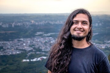 Man with long hair and a beard raising his arms in joy while standing on a mountain top with a...