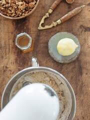 A mixer blends ingredients for baking on a rustic wooden countertop. Nearby are a bowl of granola, a jar of honey, and a pat of butter on a small dish, creating a cozy kitchen atmosphere